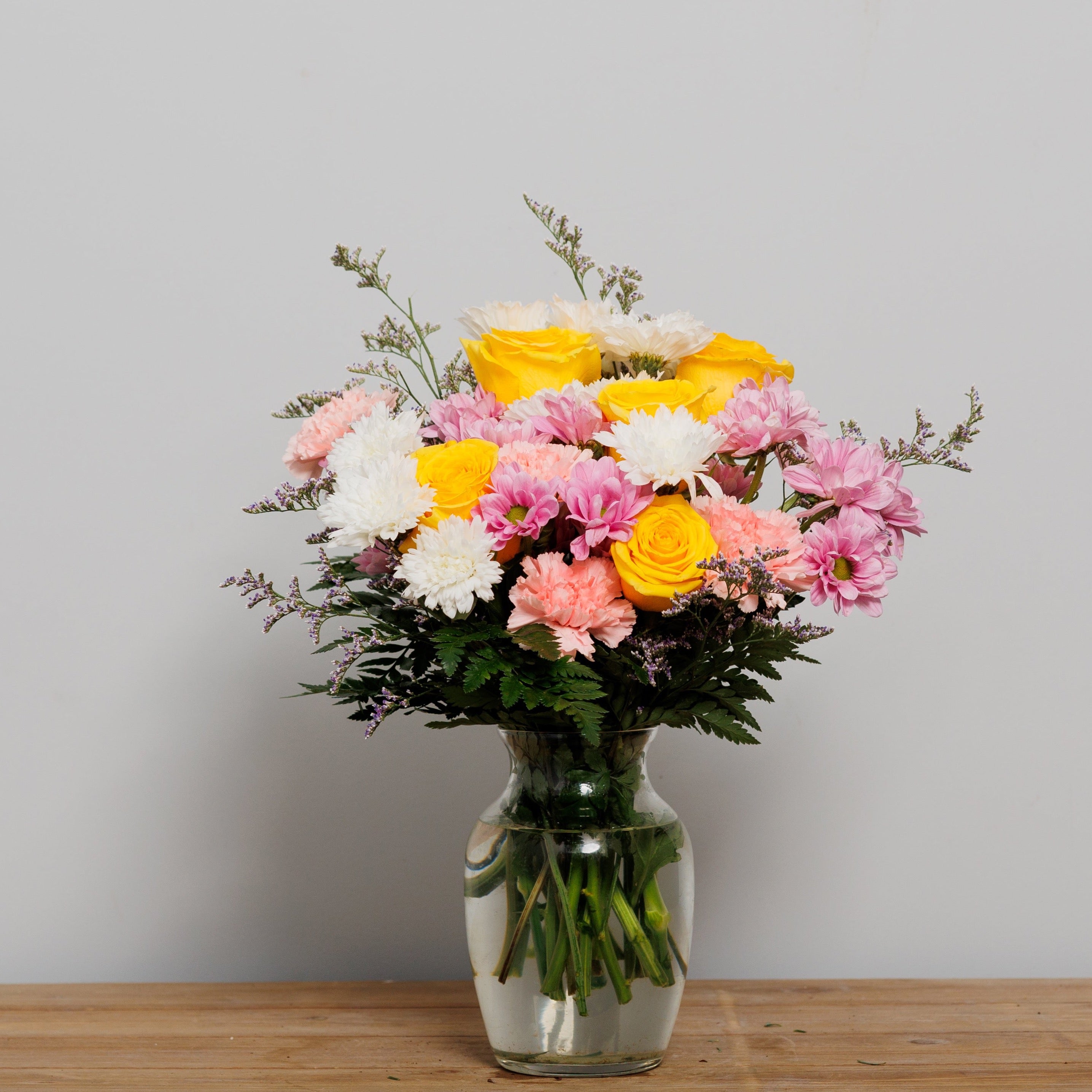 A pastel vase arrangement with yellow roses, white mums, pink carnations and lavender daisies.