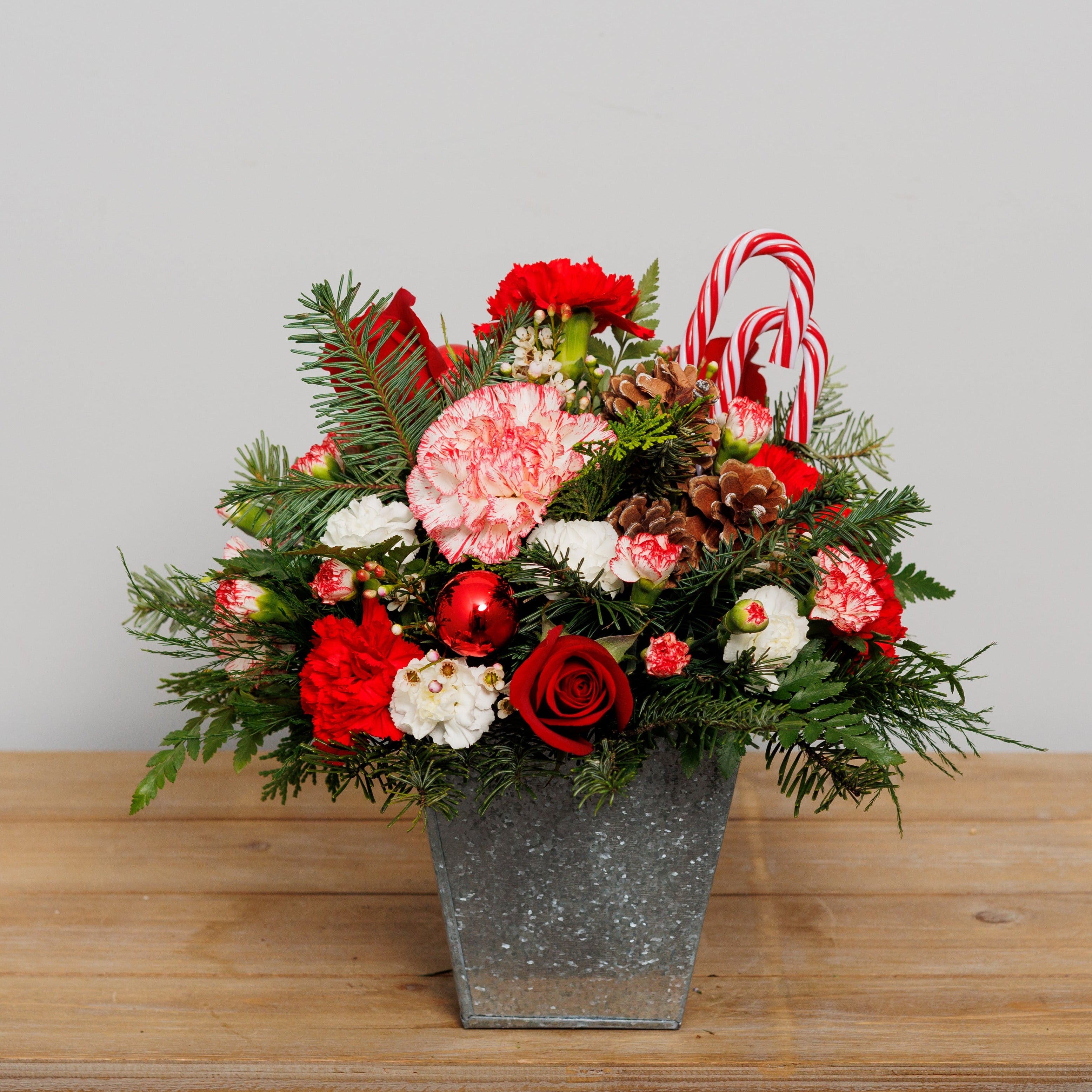 A red and white holiday arrangement in a tin container with candy canes.