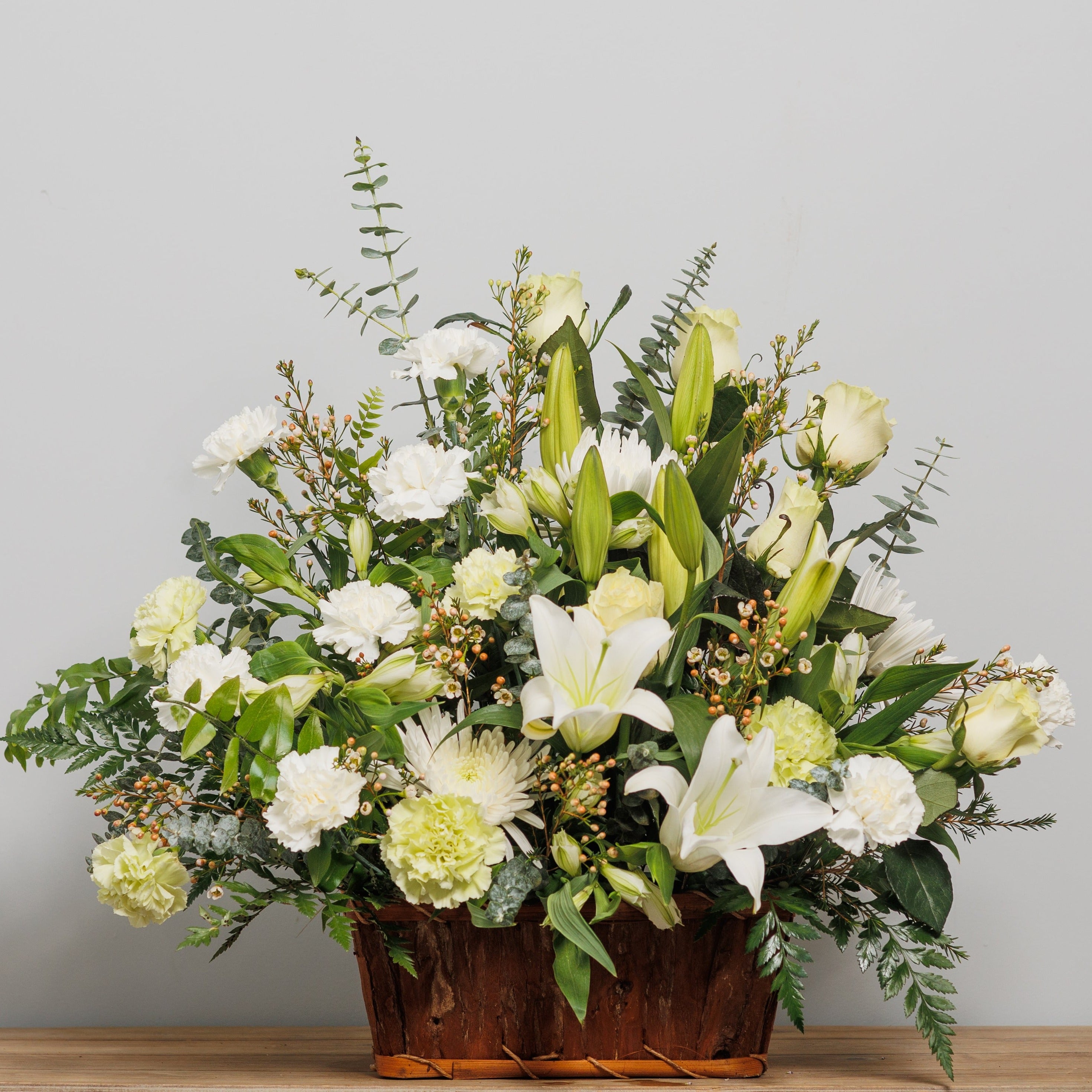 A basket arrangement with green roses and carnations and white lilies.