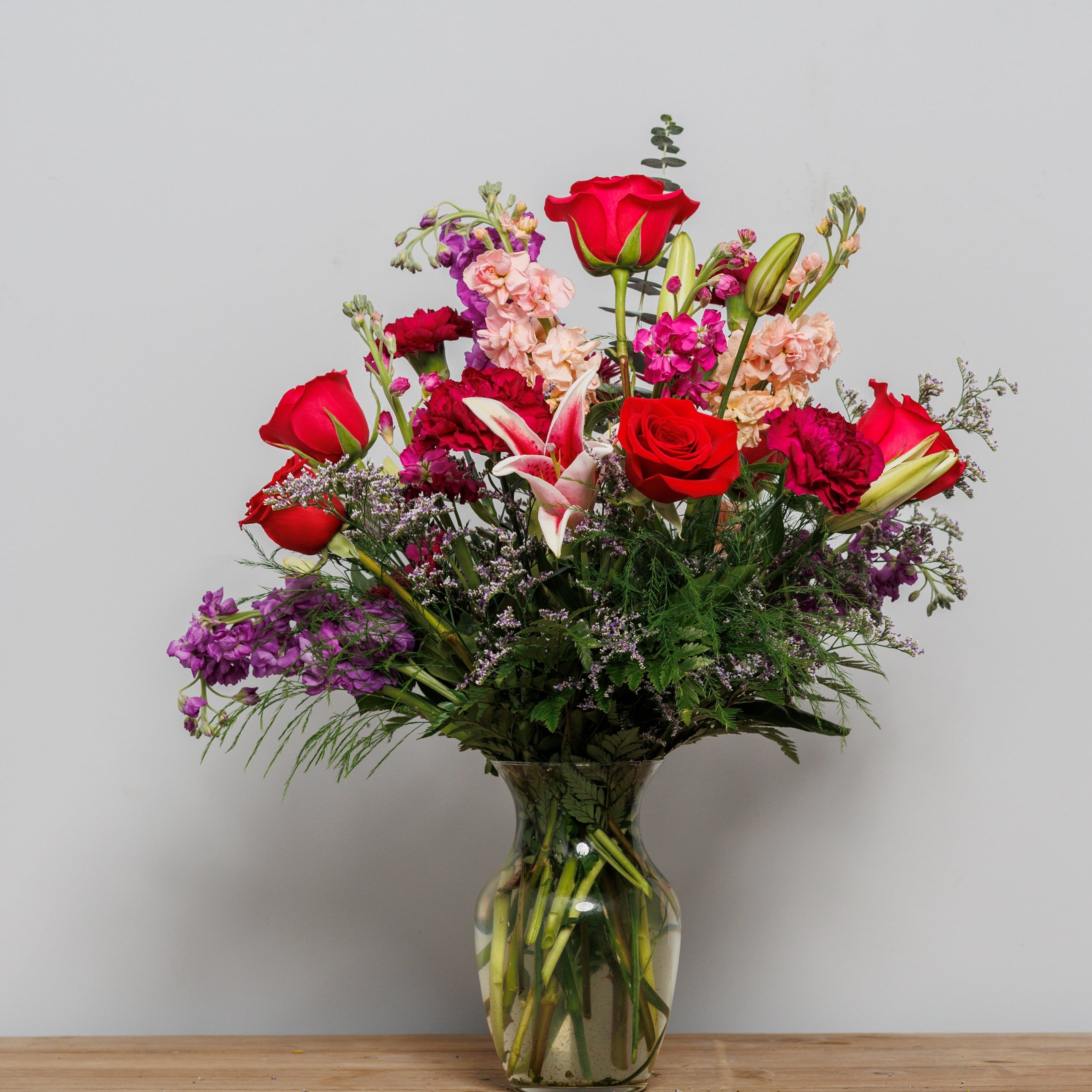 A mixed bouquet of red roses, purple stock, stargazer lilies and purple carnations.