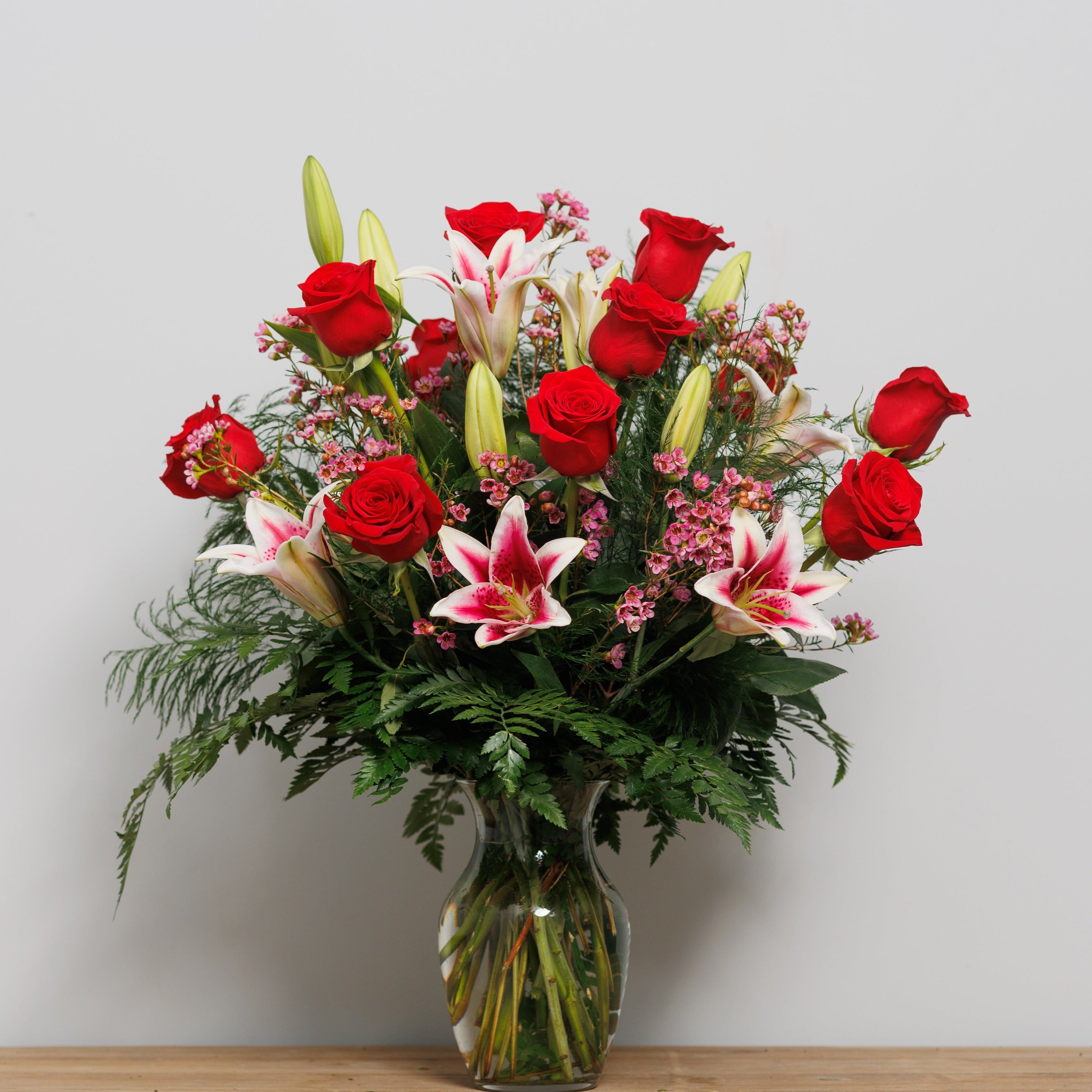 A dozen red roses with stargazer lilies in a vase.