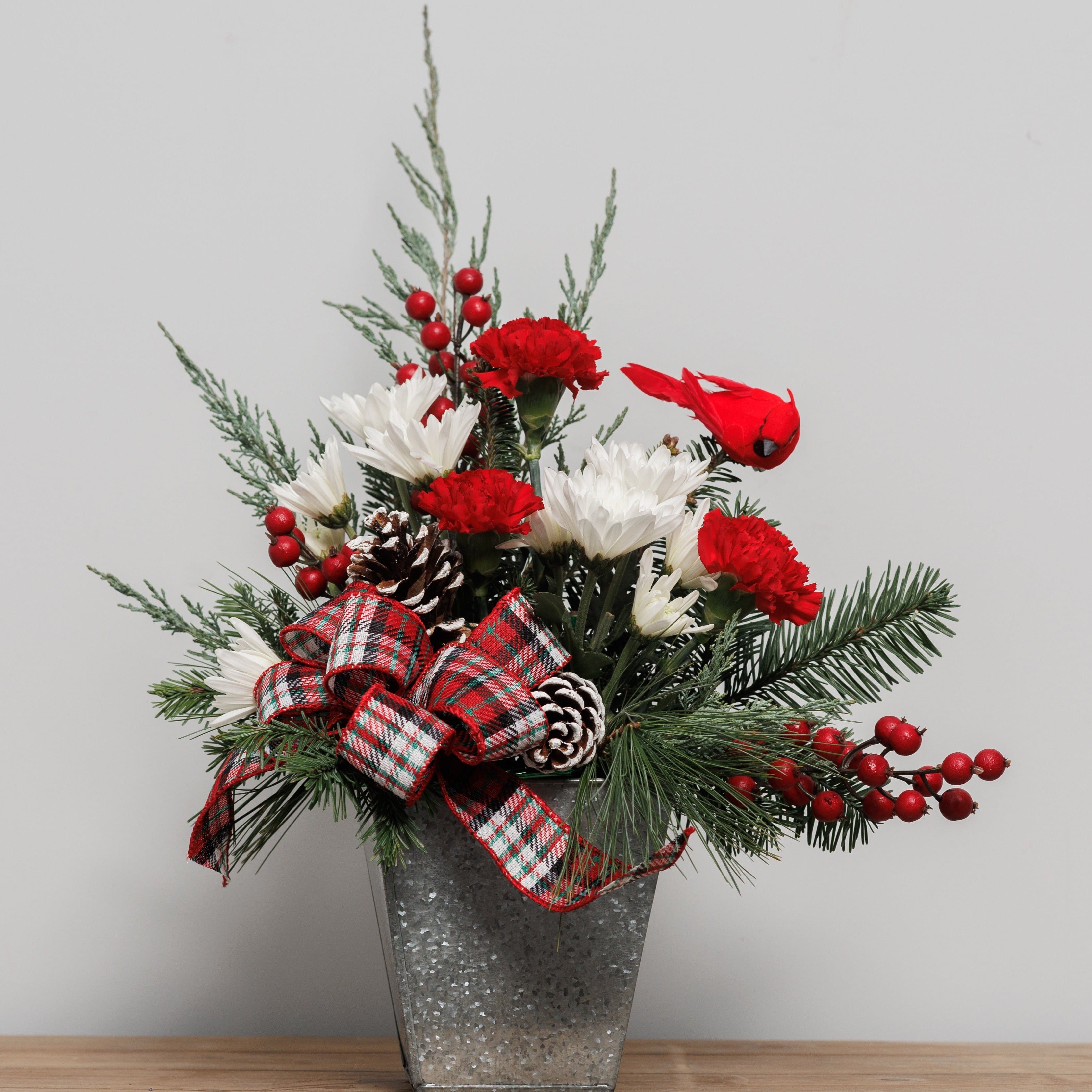 A red and white flower arrangement with pine cones and cardinal pick in a galvanized tin container.