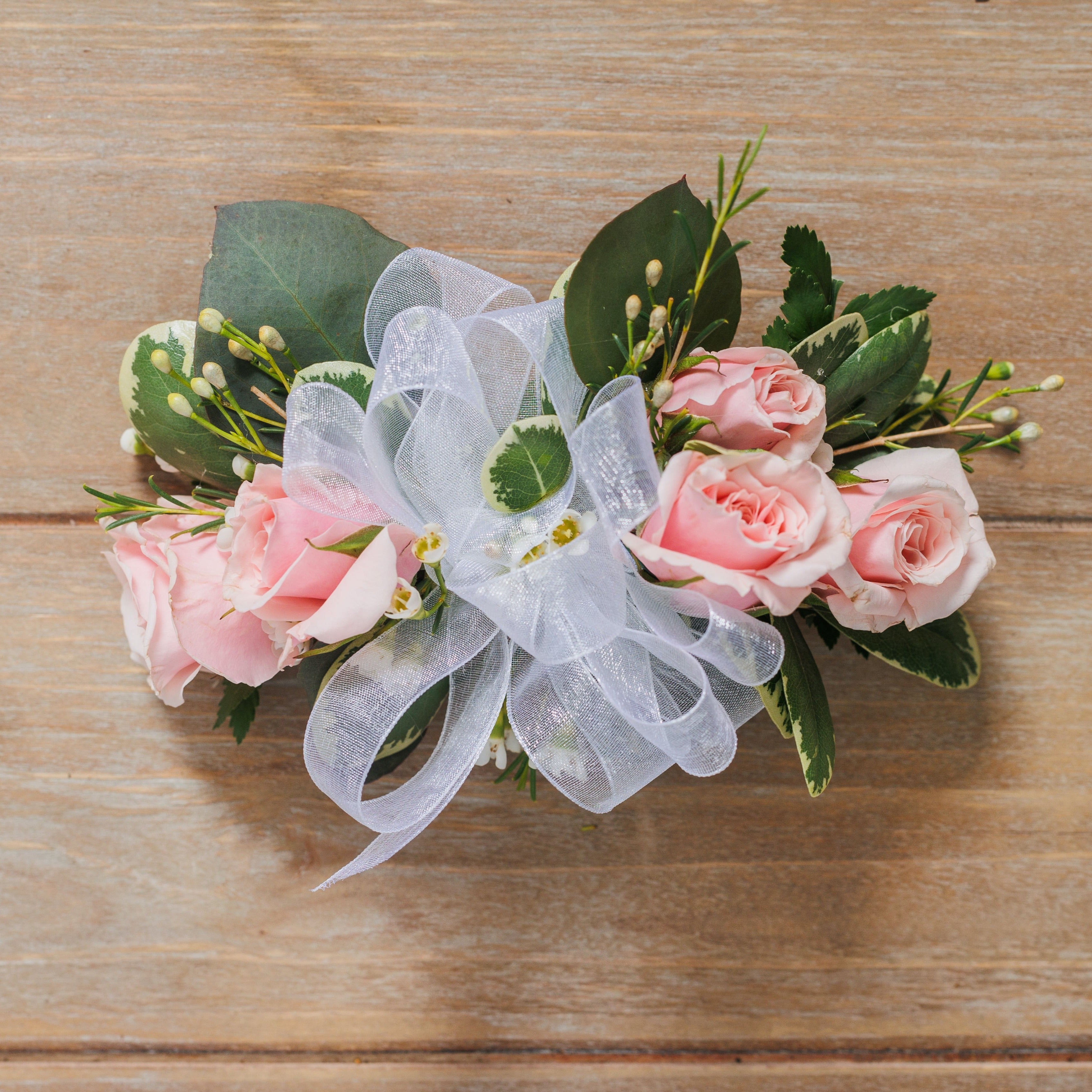 A wrist corsage with light pink spray roses and sheer white ribbon.