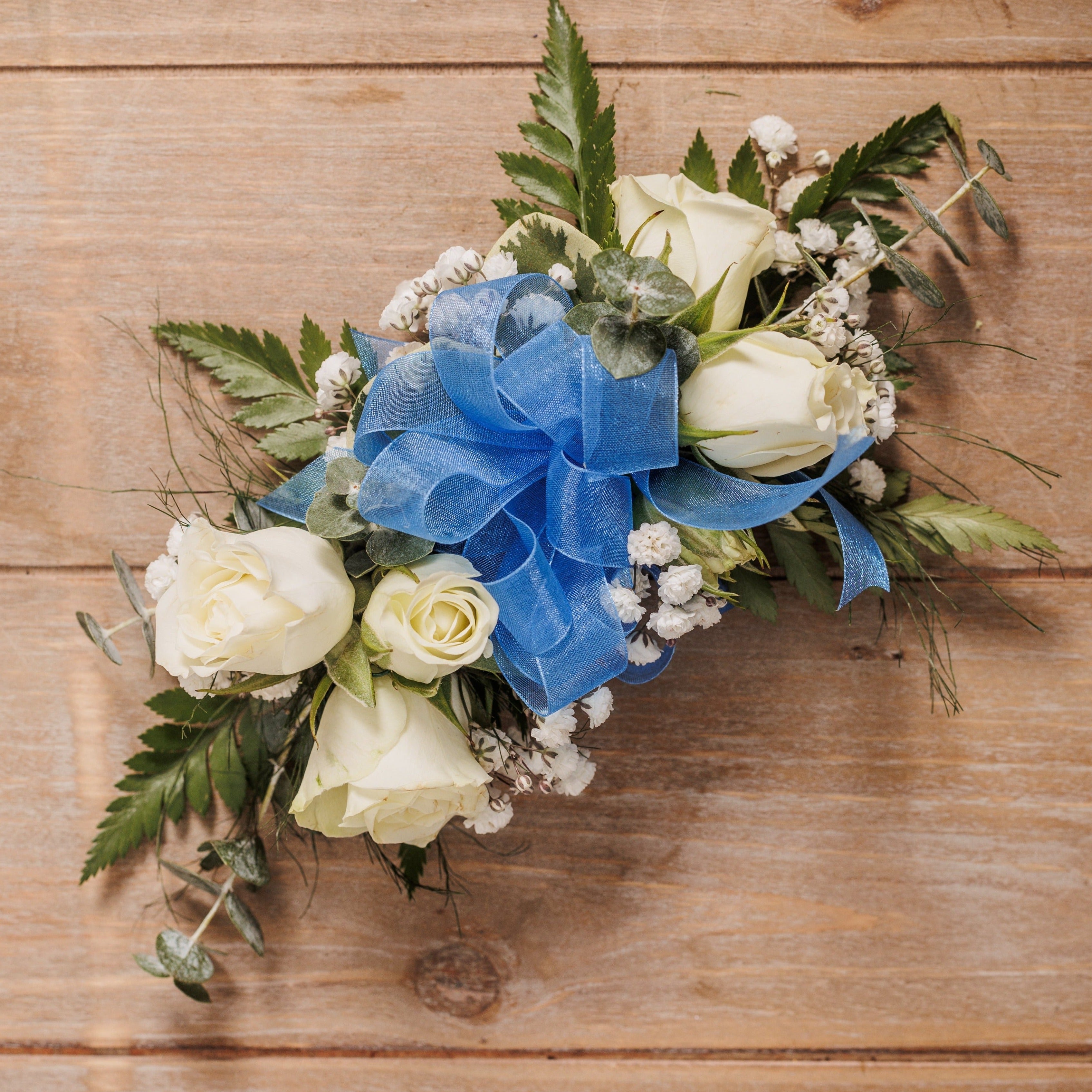 A wrist corsage with white spray roses and blue ribbon.